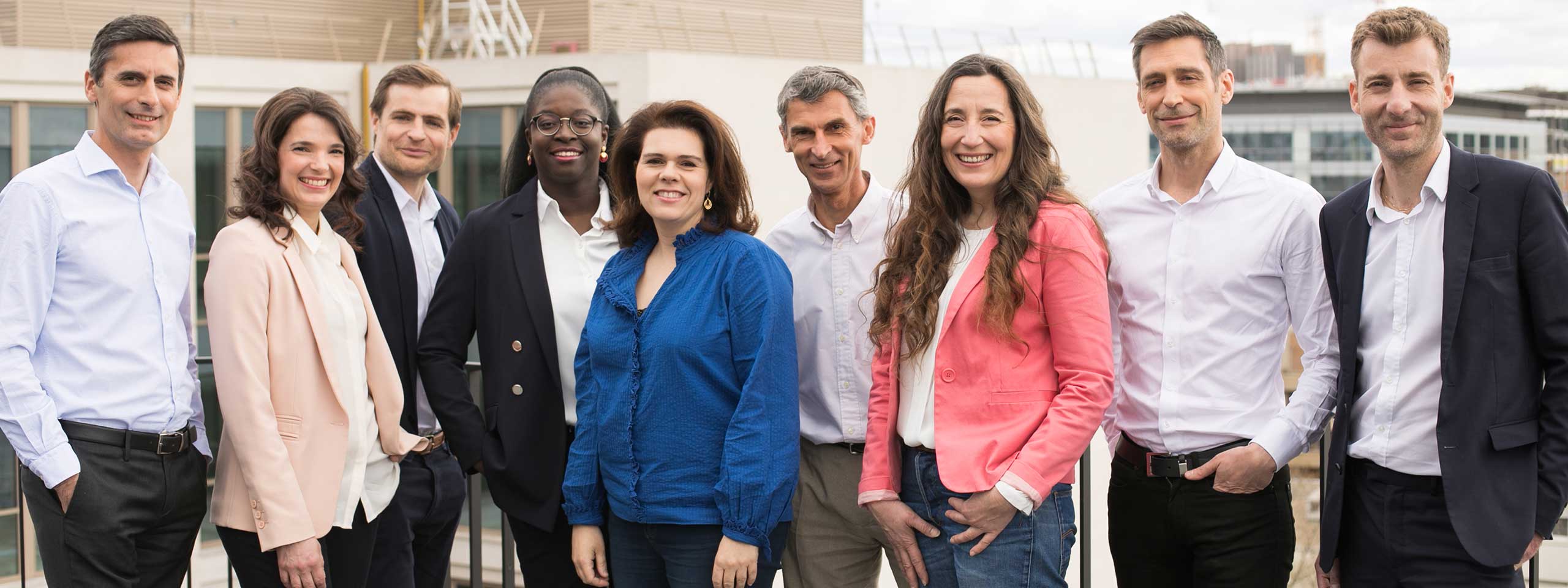 A group of professionals posing outdoors, dressed in casual attire, with a modern building in the background.