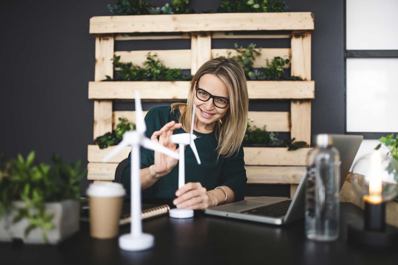 Une femme travaille à un bureau avec des éoliennes miniatures, un ordinateur portable et des plantes en arrière-plan.