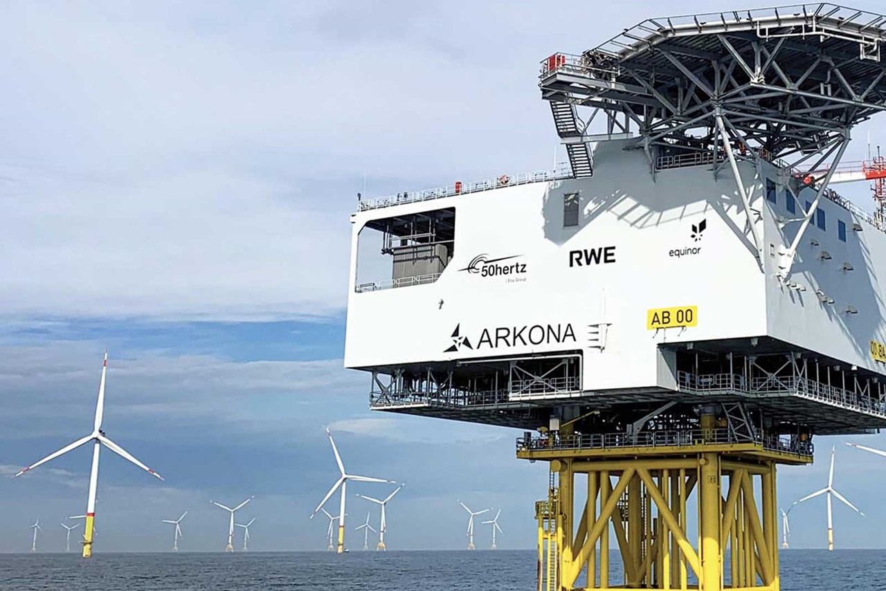 Une plateforme d'éolienne en mer avec plusieurs éoliennes en arrière-plan, sous un ciel dégagé.
