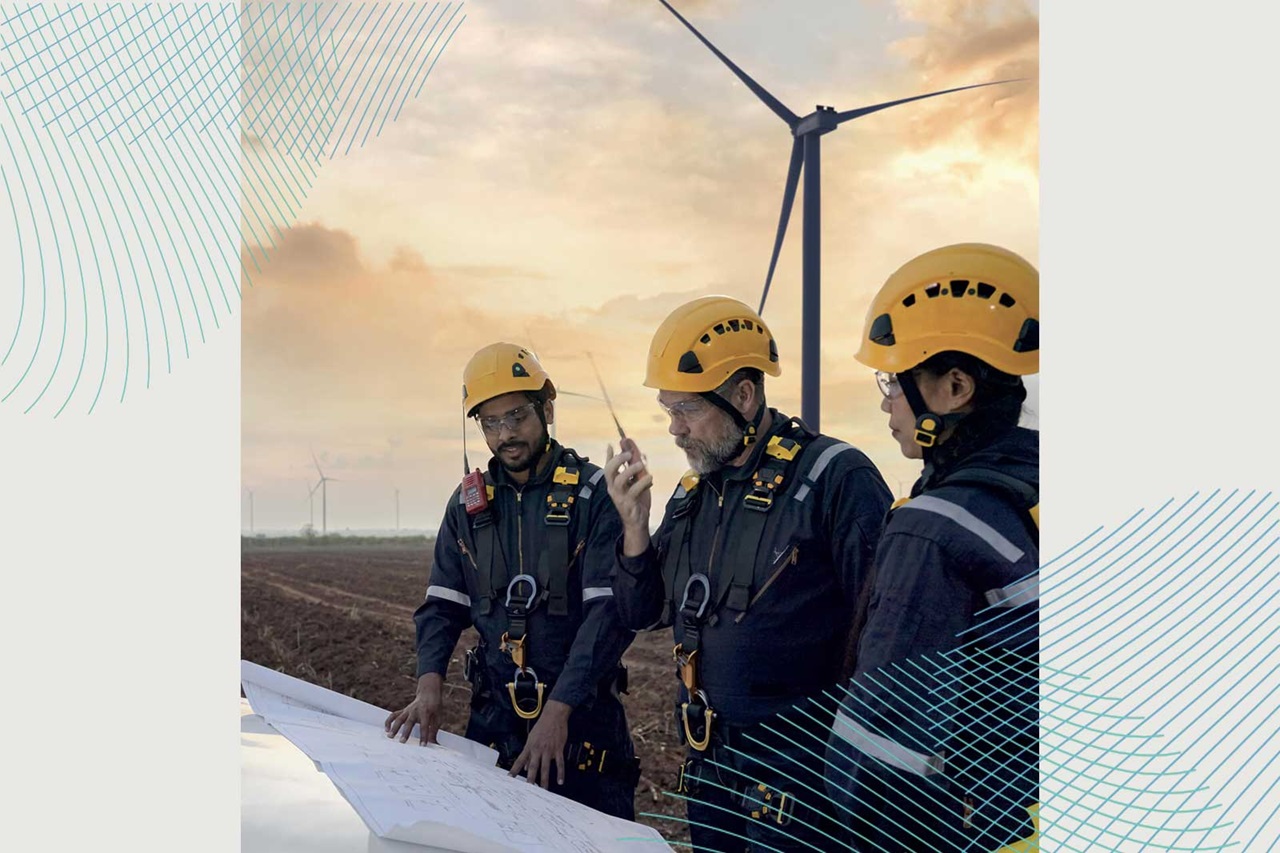 Trois travailleurs en équipement de sécurité discutent de plans dans un parc éolien, avec des éoliennes en arrière-plan.