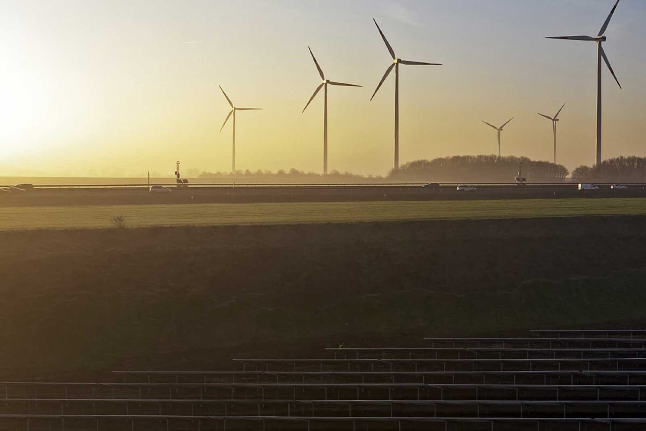 Un paysage avec des éoliennes au coucher du soleil, présentant une autoroute et des champs verts au premier plan.