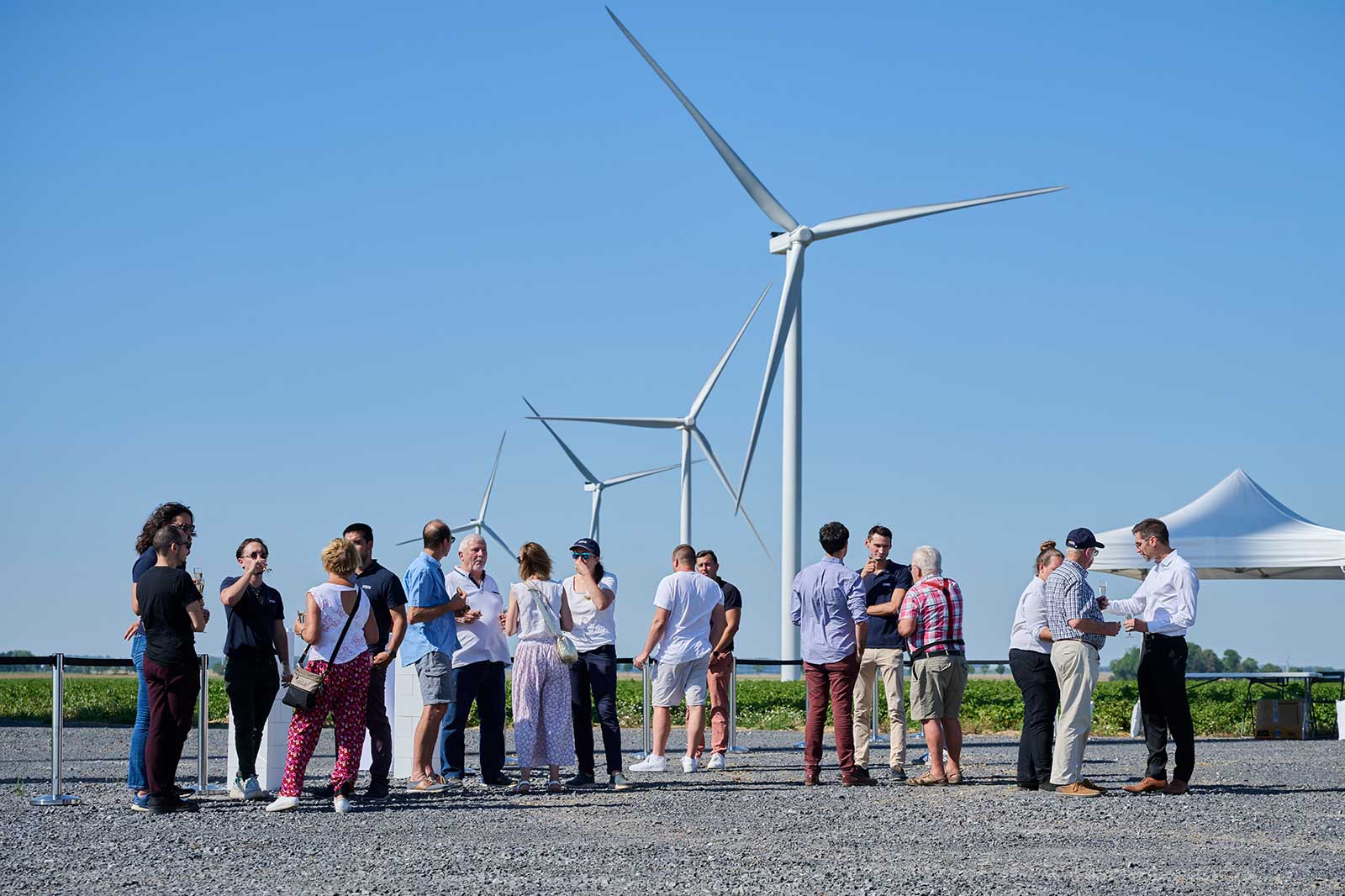 Un groupe de personnes rassemblées près d'éoliennes, discutant ensemble par une journée ensoleillée.