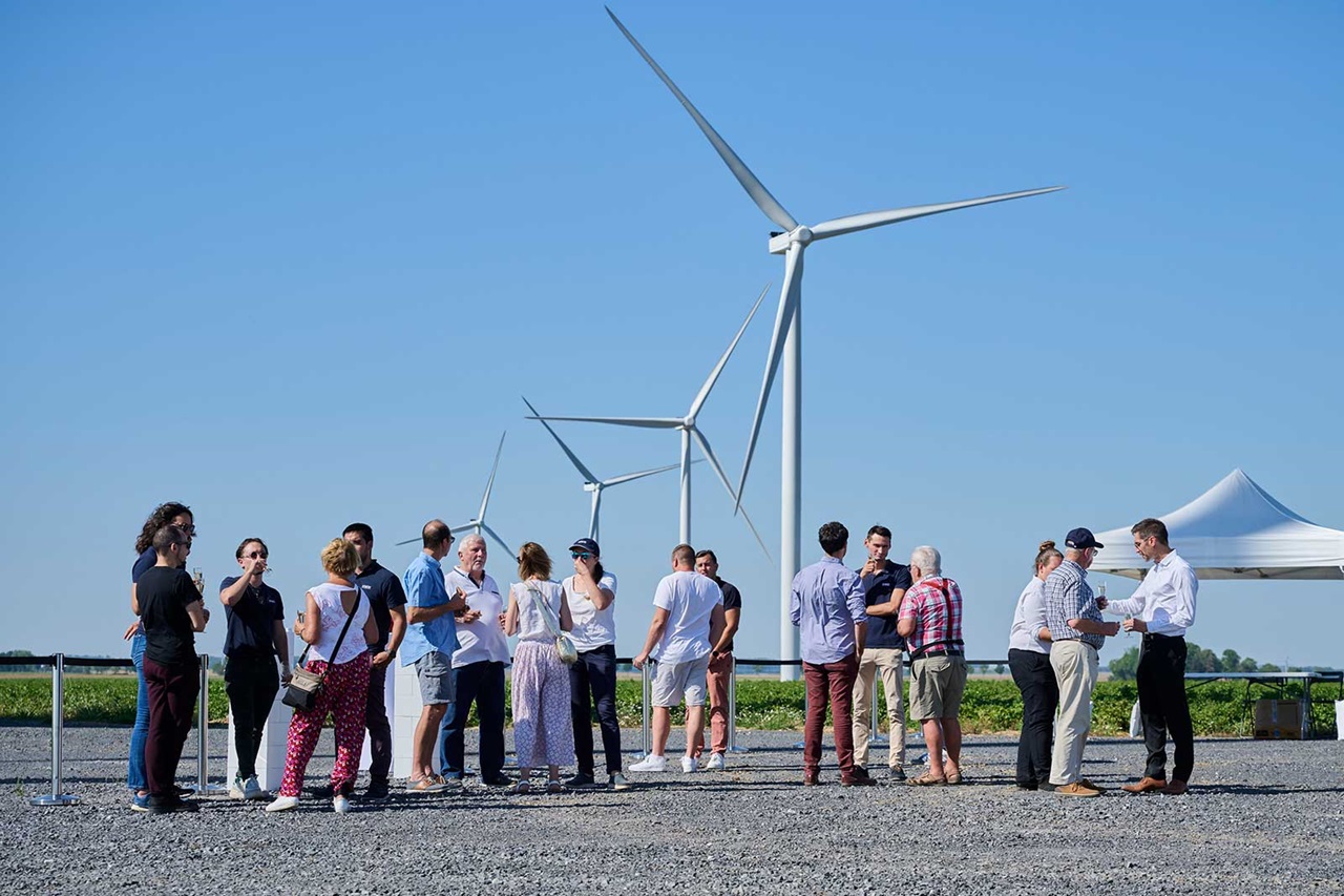 A group of people gathered near wind turbines, discussing together on a sunny day.