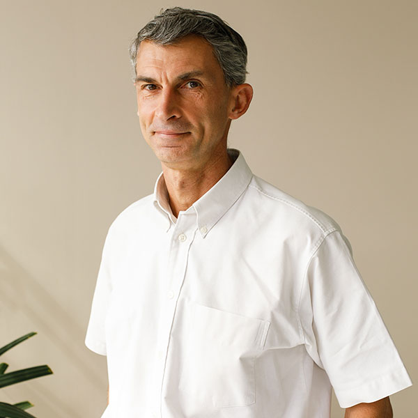 A man is wearing a white collared shirt in an indoor space, with a light background and a green plant in the corner. Portrait of Rémy Graye.