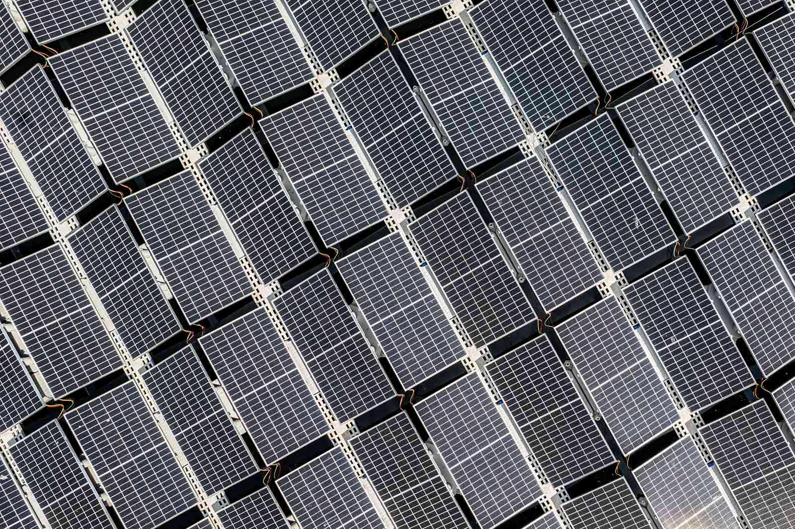 Vue aérienne de multiples panneaux solaires disposés en grille, mettant en valeur leurs surfaces réfléchissantes.