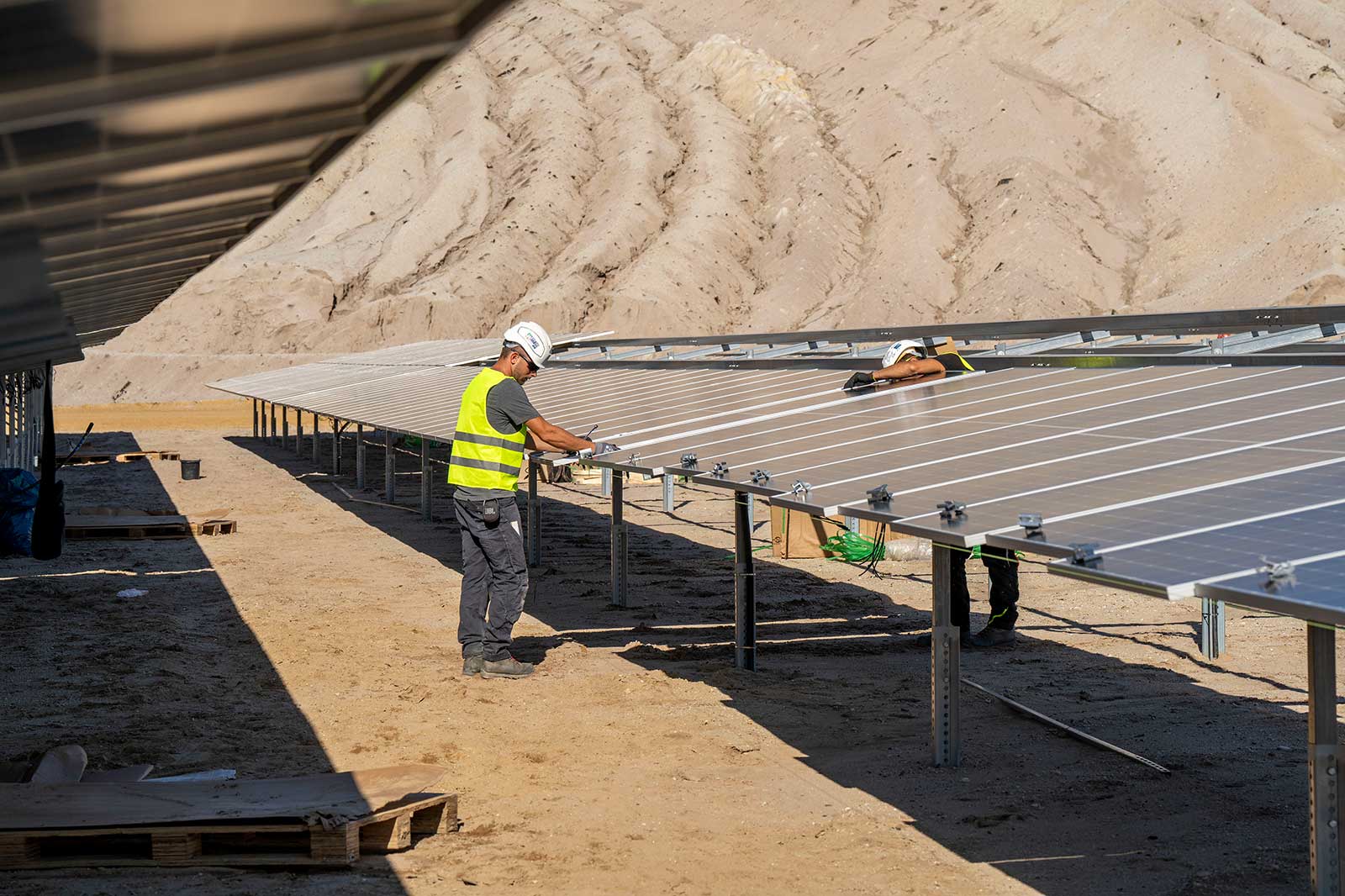 Workers are installing solar panels in a desert area under a clear blue sky, focused on their tasks.