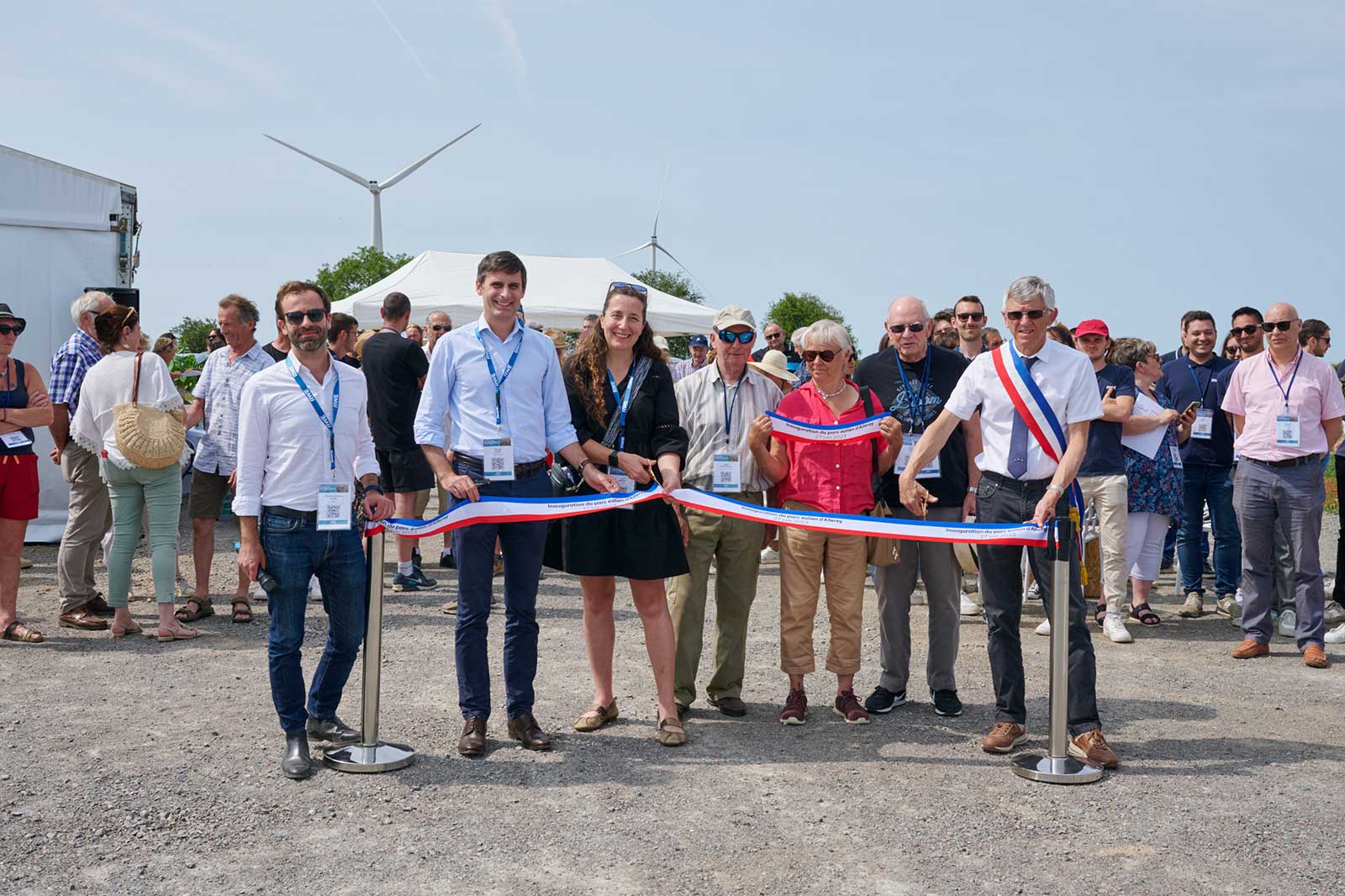 Un groupe de personnes lors d'une cérémonie d'inauguration avec une éolienne en arrière-plan et un chapiteau blanc.