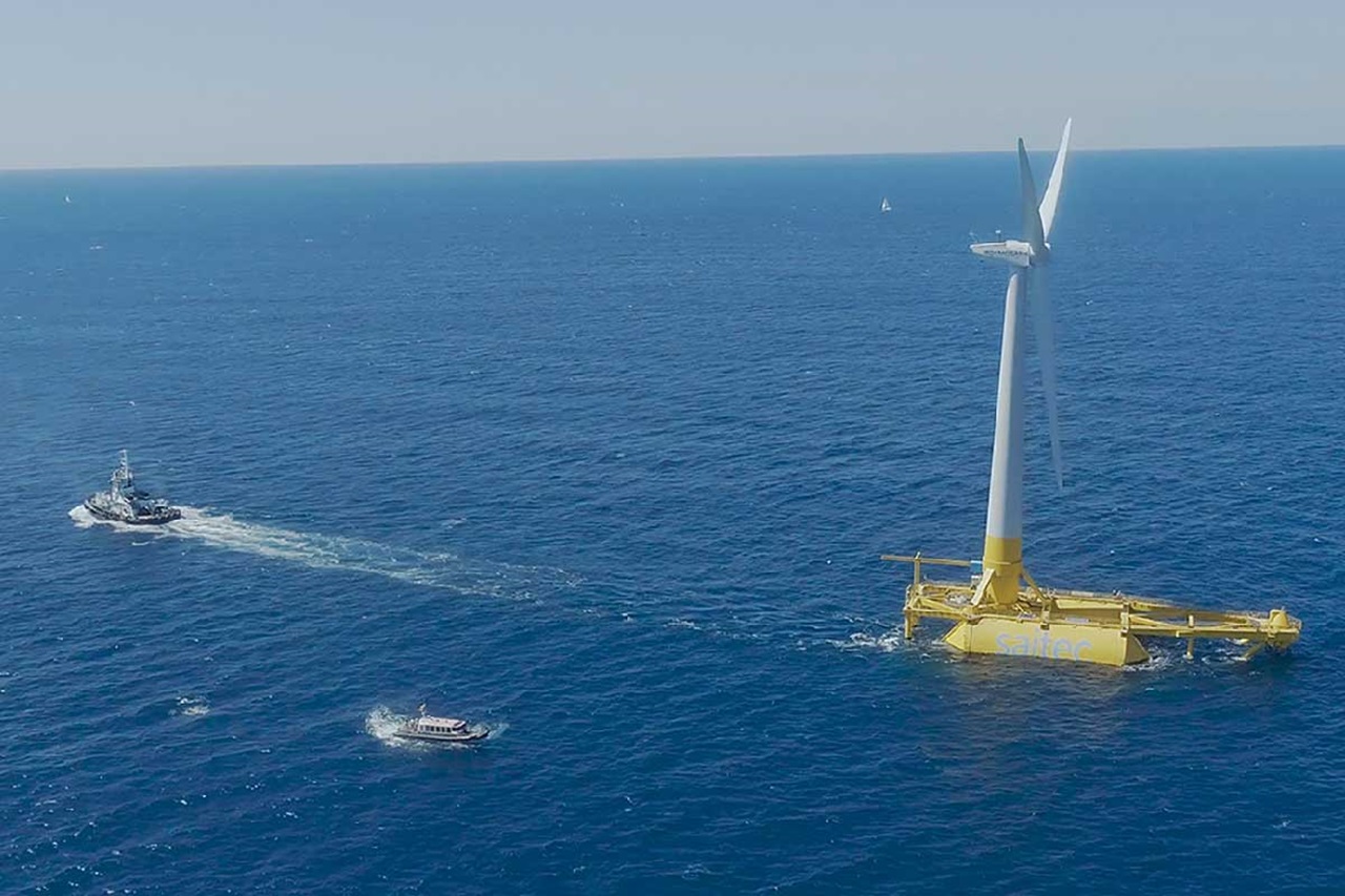An offshore wind turbine stands in the sea, with boats navigating nearby under a clear sky.