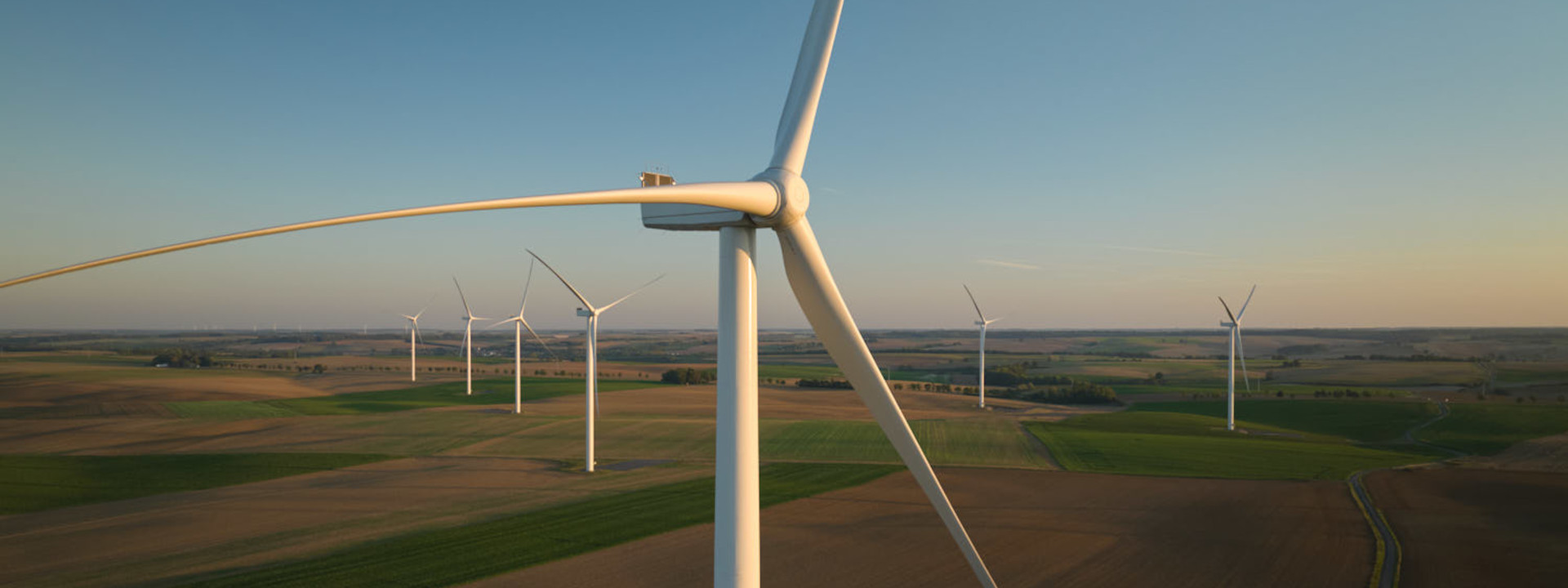 Une vue rapprochée d'une éolienne avec plusieurs autres en arrière-plan, se dressant sur un vaste paysage ouvert.