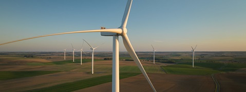 Une vue rapprochée d'une éolienne avec plusieurs autres en arrière-plan, se dressant sur un vaste paysage ouvert.
