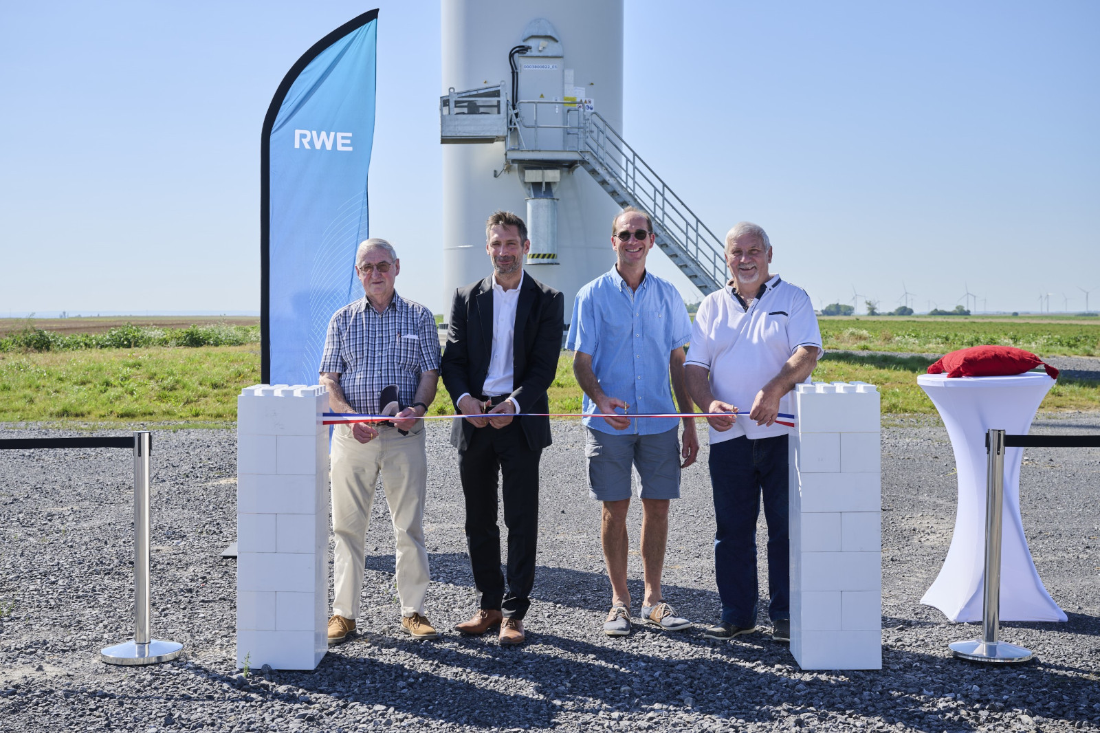 Quatre personnes participent à une cérémonie d'inauguration avec un ruban à un site d'éolienne, avec une bannière RWE en arrière-plan.