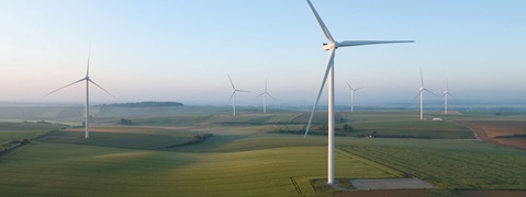 Une vue pittoresque de plusieurs éoliennes se dressant dans des champs verts sous un ciel bleu clair à l'aube.