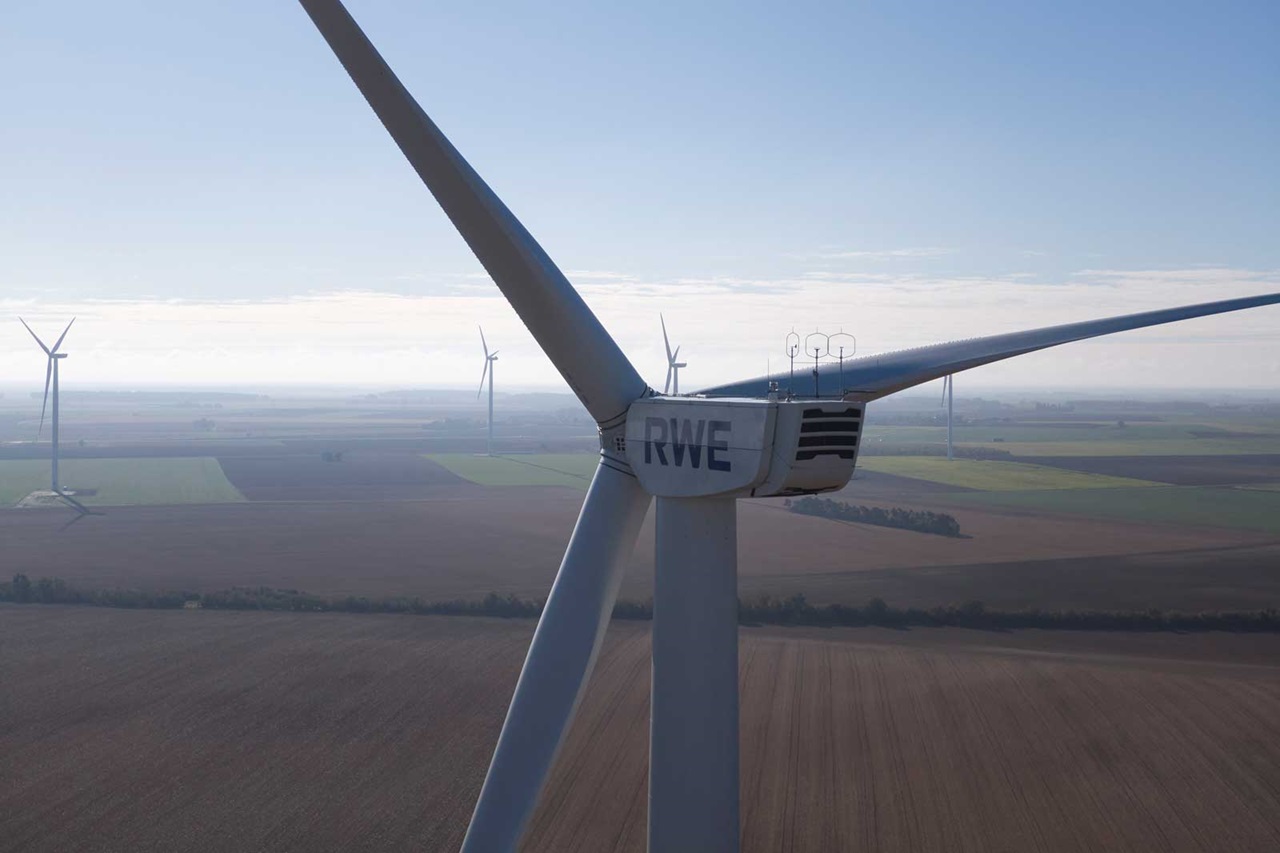 Gros plan sur une éolienne avec l'inscription RWE, avec d'autres éoliennes et des champs agricoles en arrière-plan.