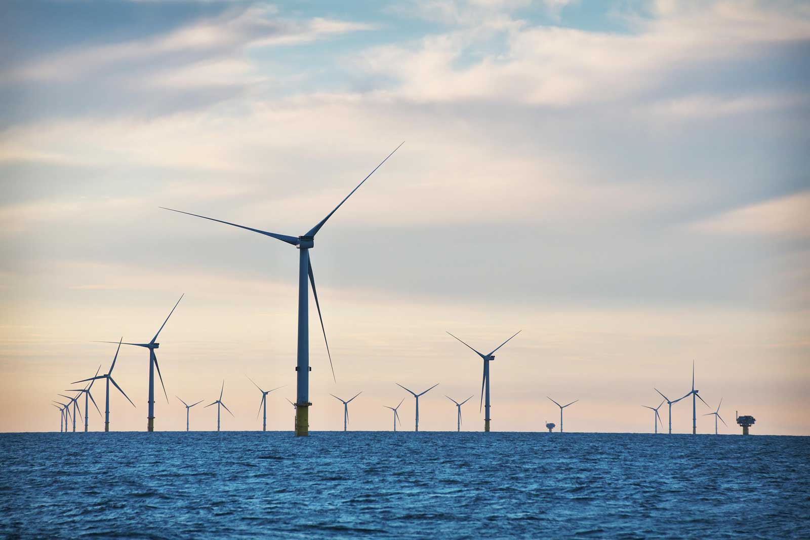 A row of wind turbines stands in the water under a partially cloudy sky.