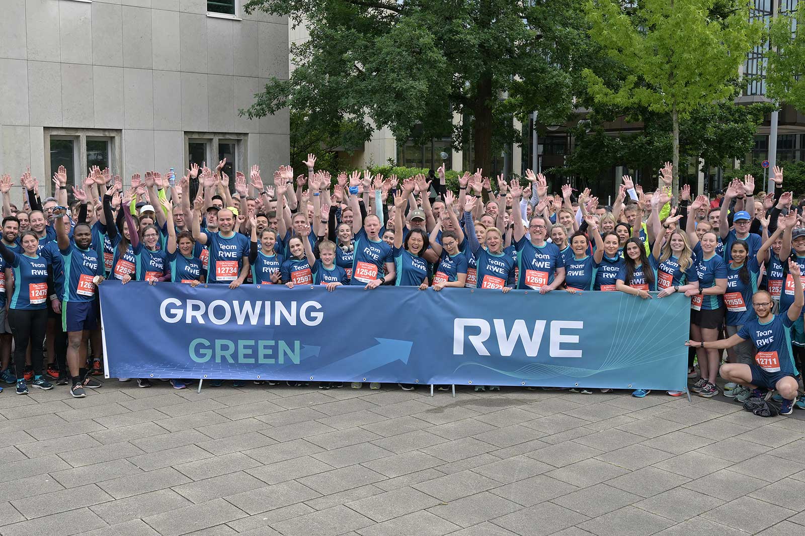 A group of runners stands with raised hands in front of a banner that reads 'Growing Green RWE'.